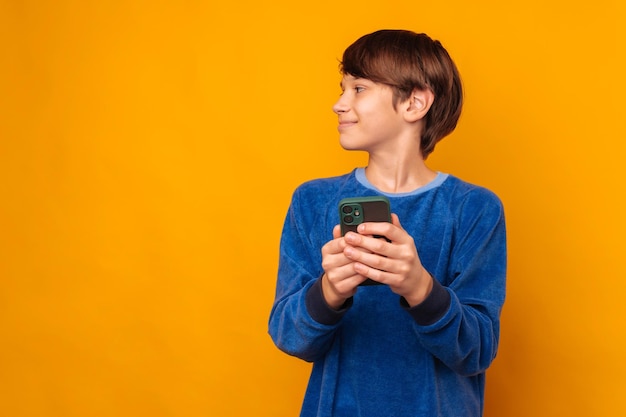 Un adolescent souriant et timide tient un téléphone et regarde de côté l'espace de copie