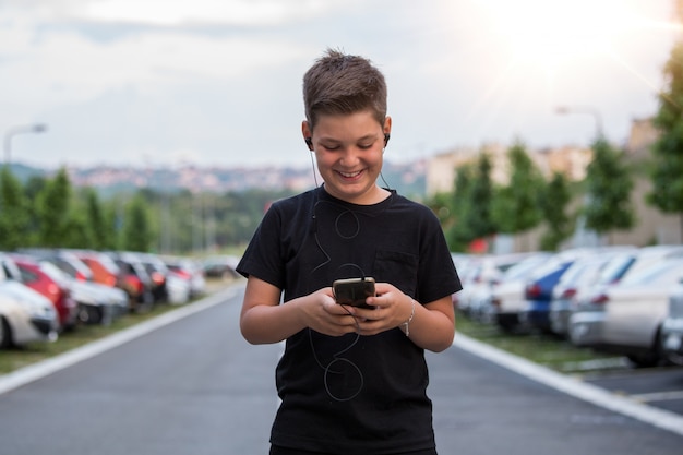 Adolescent souriant tout en envoyant des SMS à ses amis via les réseaux sociaux à l&#39;aide d&#39;un téléphone portable, assis contre un paysage urbain