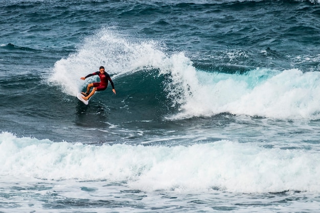 Adolescent surfant à la vague à tenerife playa de las americas - combinaisons rouges et belle et parfaite vague - freestyle et faire des tours