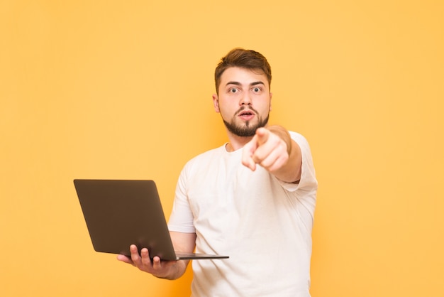 Adolescent surpris dans un T-shirt blanc est debout sur le jaune avec un ordinateur portable dans ses mains