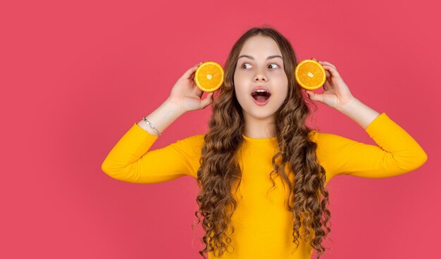 un adolescent surpris tient des fruits orange sur fond rose