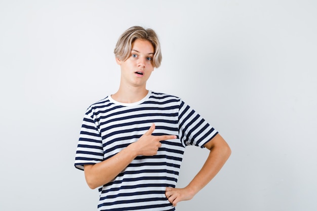 Adolescent en t-shirt pointant vers le côté droit, ouvrant la bouche et l'air choqué, vue de face.