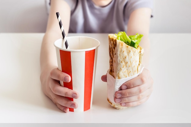 Adolescent tenant un sandwich au shawarma et une boisson gazeuse sucrée.