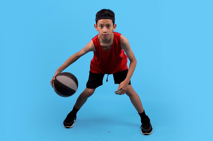 Un adolescent en tenue de sport rouge drible le basket-ball alors qu'il s'entraîne dans un studio
