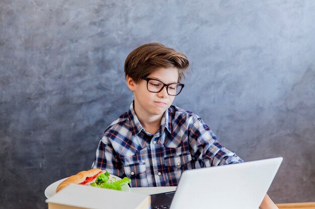 Adolescent triste utilisant un ordinateur portable et prenant son petit déjeuner