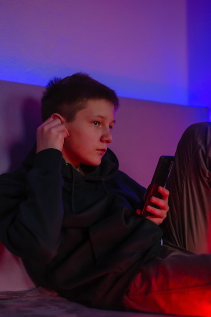 Adolescent utilisant un téléphone et un casque dans sa chambre avec néon