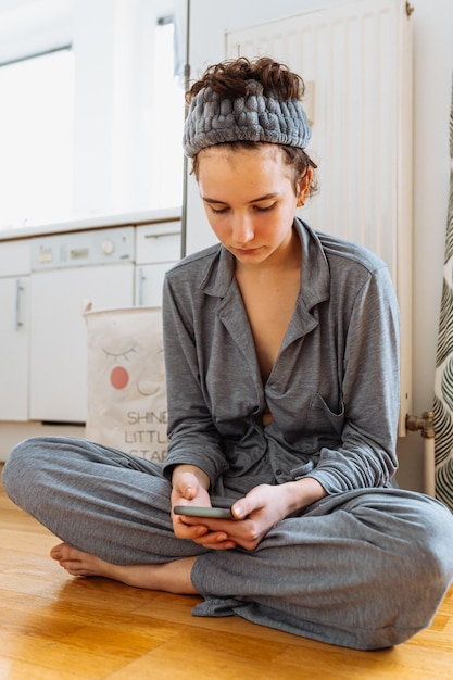 adolescent vérifie les notifications sur smartphone, blogs sur Internet, connecté au Wi-Fi, est assis sur le sol