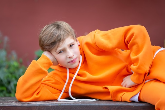 Photo un adolescent vêtu d'orange pose allongé sur un banc