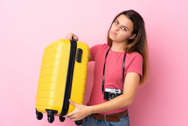 Adolescent voyageur fille tenant une valise sur rose isolé avec une expression triste