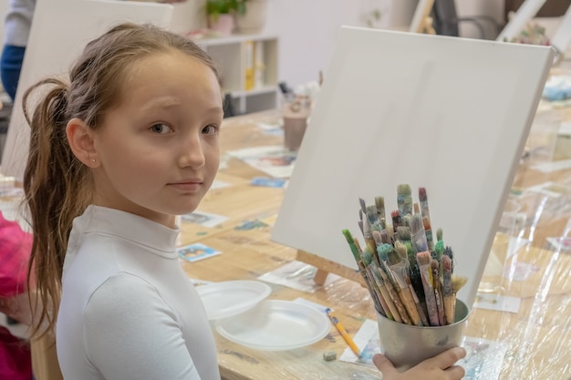 Adolescente de 9 ans assise à une table devant le chevalet et regardant la caméra. Concept de créativité et de personnes.