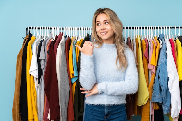 Adolescente acheter des vêtements isolés sur le mur bleu pointant vers le côté pour présenter un produit