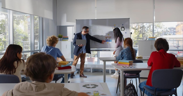 Une adolescente afro-américaine étudiante et enseignante ayant une présentation en classe sur l'environnement Vue arrière d'écoliers assis au bureau ayant une leçon d'écologie