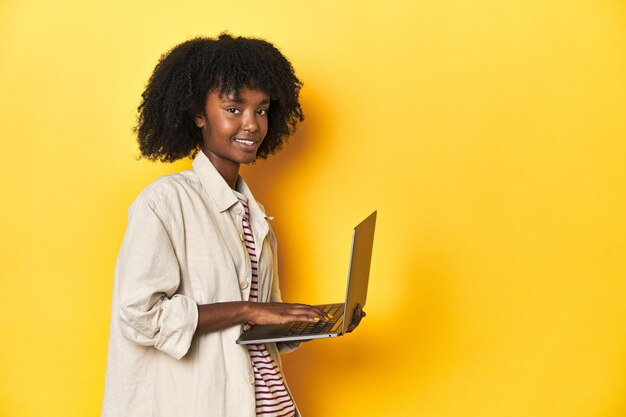 Une adolescente afro-américaine expérimentée avec un ordinateur portable sur un fond de studio jaune