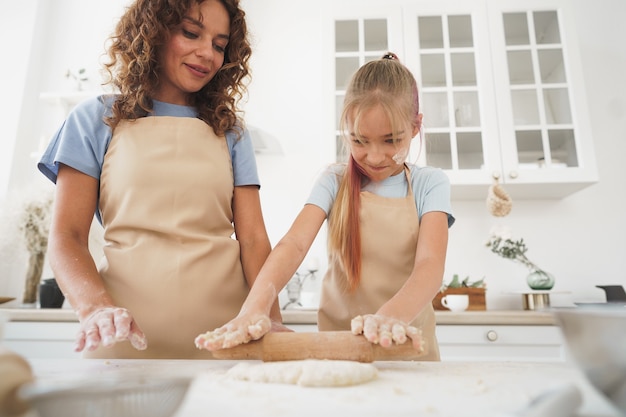 Une adolescente aide sa mère à cuisiner de la pâte dans sa cuisine à la maison