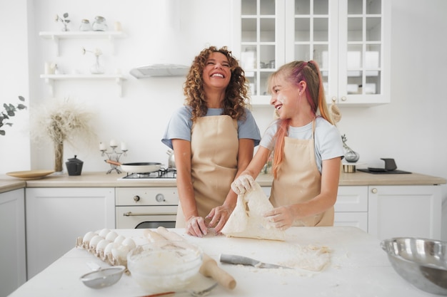 Une adolescente aide sa mère à cuisiner de la pâte dans sa cuisine à la maison