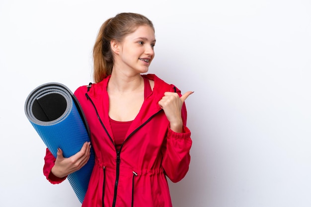 Adolescente allant à des cours de yoga tout en tenant un tapis isolé sur fond blanc pointant vers le côté pour présenter un produit