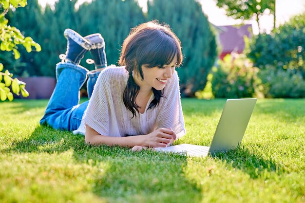 Adolescente allongée sur l'herbe à l'aide d'un ordinateur portable