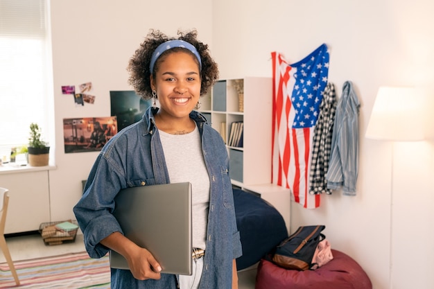 Une adolescente américaine joyeuse avec un ordinateur portable debout dans sa chambre