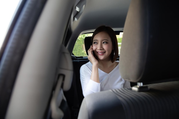 Une adolescente asiatique appelle sur son smartphone sur le siège arrière d'une voiture.