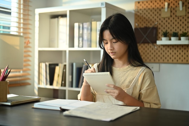 Une adolescente asiatique concentrée fait ses devoirs, un projet scolaire, se prépare à l'examen à la maison.