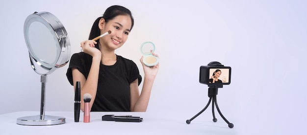 Photo une adolescente asiatique est assise devant la caméra et diffuse en direct en tant qu'influenceuse blogueuse beauté ou youtubeuse pour revoir ou donner des conseils sur la façon de se maquiller à la maison.