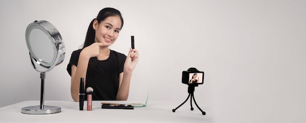 Une adolescente asiatique est assise devant la caméra et diffuse en direct en tant qu'influenceuse blogueuse beauté ou youtubeuse pour revoir ou donner des conseils sur la façon de se maquiller à la maison.