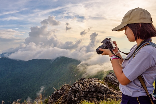 Une adolescente asiatique de randonneur porte des casquettes à la recherche d'une photo sur un appareil photo numérique est un beau paysage naturel de la sierra et du ciel pendant le coucher du soleil sur la montagne au parc forestier de Phu Chi Fa, Chiang Rai, Thaïlande