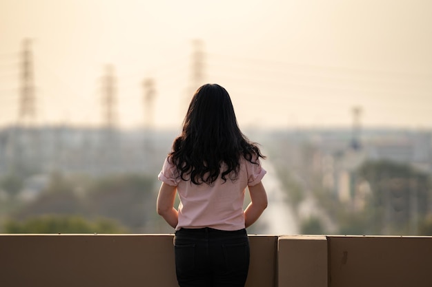 Une adolescente asiatique se tient à l'arrière devant la vue sur la ville sur le toit de l'immeuble