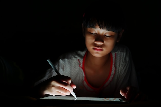 Adolescente asiatique avec tablette en tirant en position couchée sur le lit