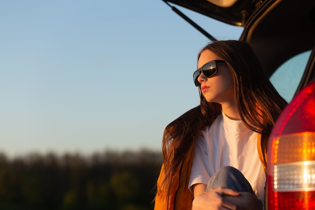 Adolescente assez triste avec des lunettes de soleil assise seule dans un coffre de voiture