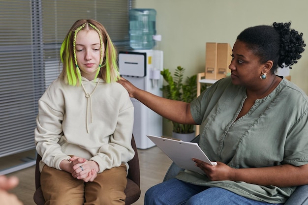 Photo adolescente assise sur une chaise et parlant avec un spécialiste lui donnant un conseil pendant le cours de thérapie