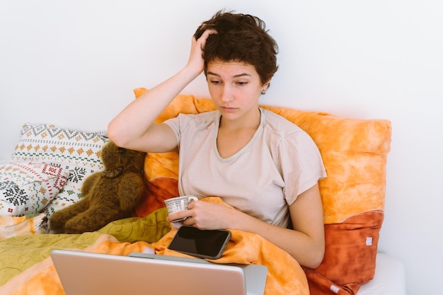 Une adolescente au lit allongée avec un ordinateur portable