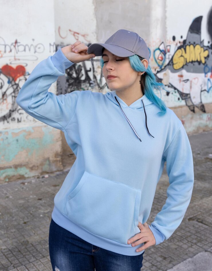 Photo adolescente aux cheveux bleus en sweat à capuche bleu et casquette de baseball avec les yeux fermés touchant sa casquette adolescente aux cheveux bleus reste à l'extérieur contre le mur de graffitis maquette de vêtements et de casquette