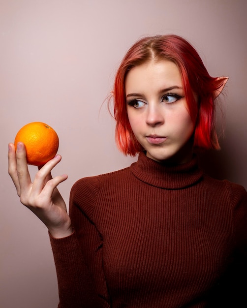 Adolescente aux cheveux roses tenant une orange dans sa main