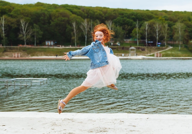 Adolescente aux cheveux rouges sautant et s'amusant sur la plage pendant la journée