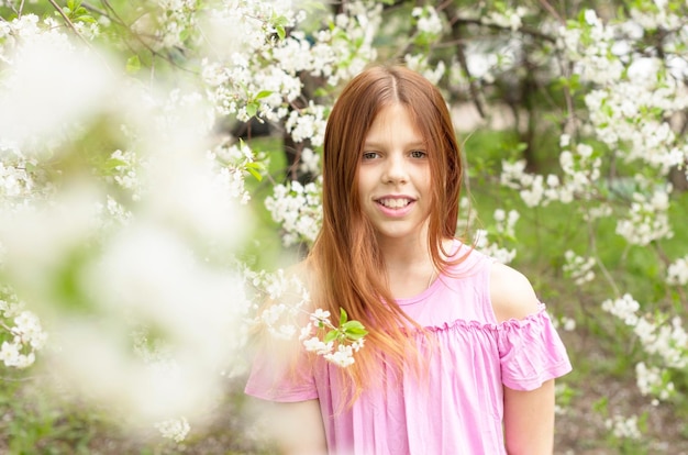 Adolescente aux cheveux roux s'amusant dans un verger de cerisiers en fleurs le concept du printemps et la fin de la quarantaine