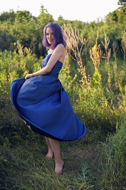 Adolescente aux cheveux teints en violet et un piercing au nez dans l'herbe avec une robe bleue