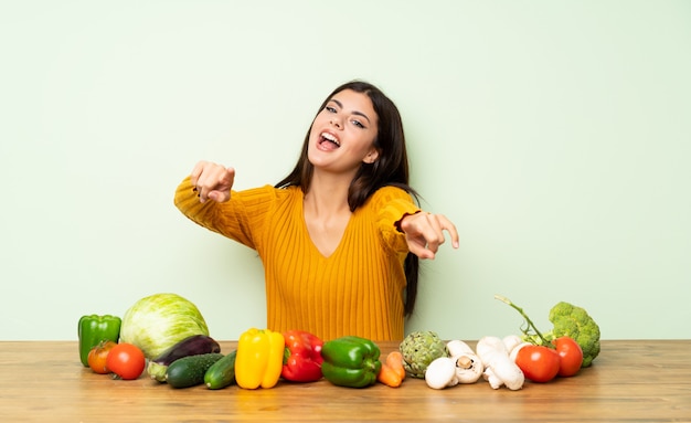 Une adolescente avec beaucoup de légumes pointe le doigt vers vous en souriant