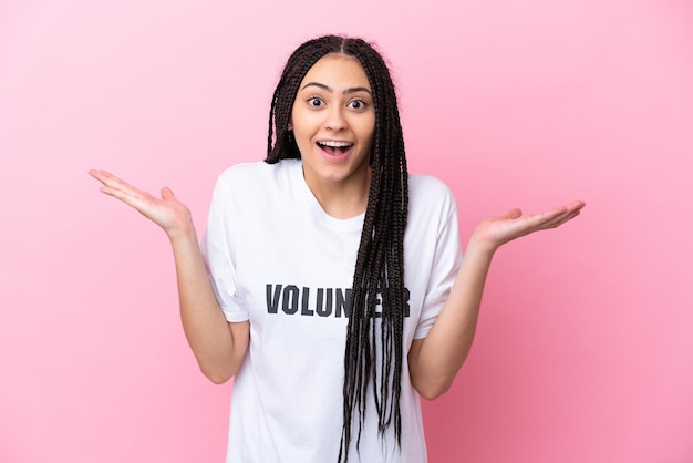 Adolescente bénévole avec des tresses isolées sur fond rose avec une expression faciale choquée