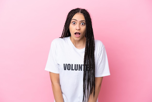 Adolescente bénévole avec des tresses isolées sur fond rose avec une expression faciale surprise