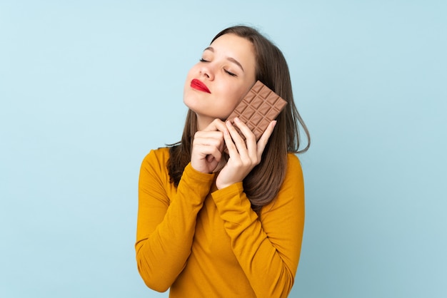 Adolescente sur bleu en prenant une tablette de chocolat et heureux