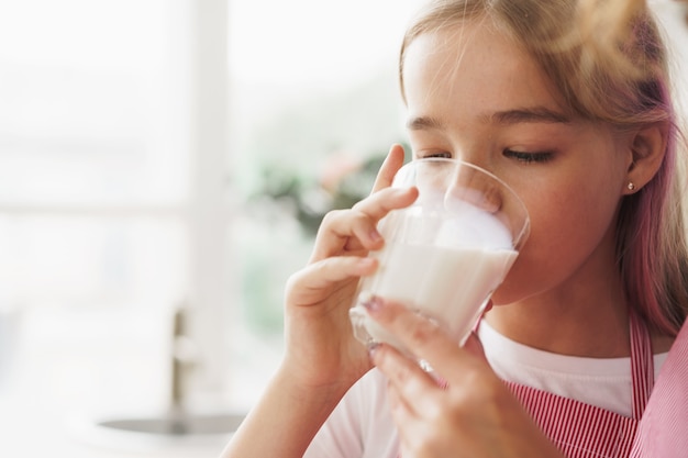 Adolescente blonde buvant un verre de lait à la maison dans la cuisine