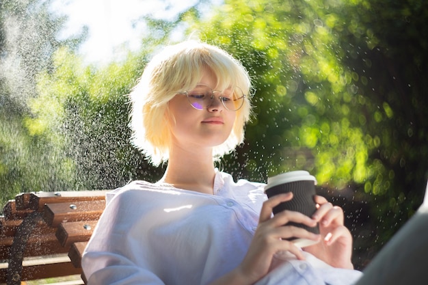 Adolescente avec blonde entendre boire du café à partir d'une tasse de papier kraft à l'extérieur