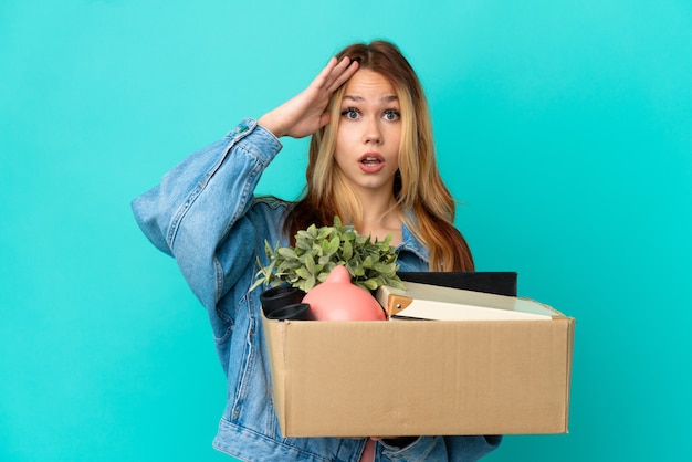 Adolescente blonde faisant un geste tout en ramassant une boîte pleine de choses avec une expression de surprise