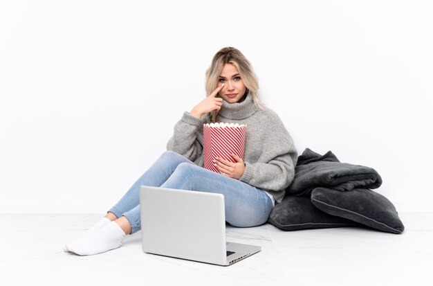 Adolescente blonde femme mangeant du pop-corn tout en regardant un film sur l'ordinateur portable