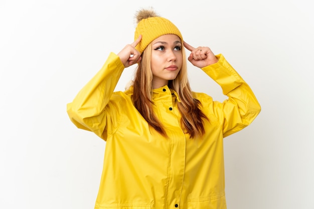 Adolescente blonde portant un manteau imperméable sur fond blanc isolé ayant des doutes et pensant