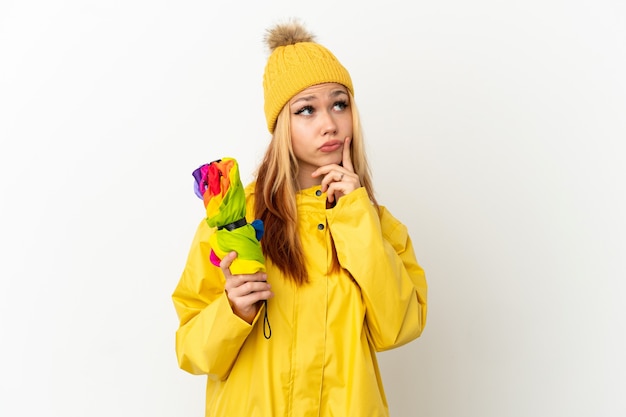 Adolescente blonde portant un manteau imperméable sur fond blanc isolé ayant des doutes tout en levant