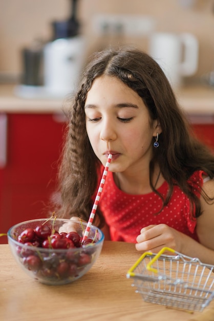 Une adolescente boit du jus d'une cerise dans une assiette à travers une paille Le concept d'une boisson naturelle biologique