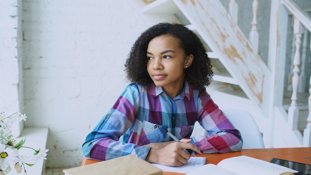 Adolescente bouclée assise à la table concentrant des leçons d'apprentissage ciblées pour l'examen