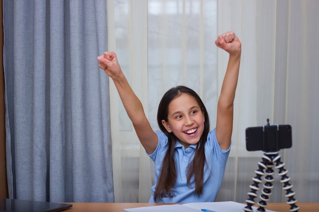 Une adolescente brune sourit à la tête d'un blog en ligne fait des cours en ligne lève joyeusement la main